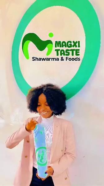 A customer with her Magxi shawarma in front of the branded wall